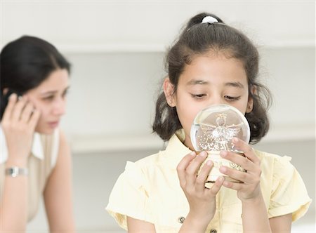 Gros plan d'une jeune fille regardant un globe de neige et sa mère parler sur un téléphone mobile derrière elle Photographie de stock - Premium Libres de Droits, Code: 630-02220324