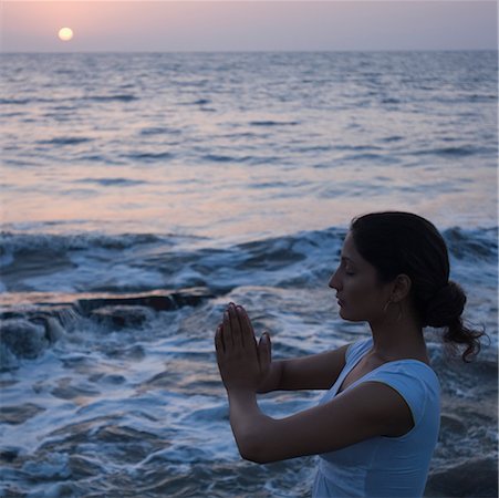 Side profile of a young woman meditating in a prayer position on the beach, Mud Island, Mumbai, Maharashtra, India Stock Photo - Premium Royalty-Free, Code: 630-02220399