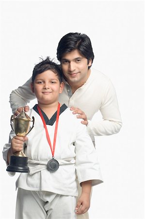 Portrait of a boy holding a trophy with his father standing behind him Stock Photo - Premium Royalty-Free, Code: 630-02220545