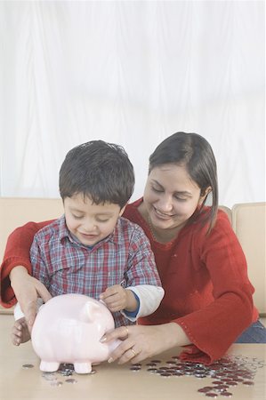 Garçon de mettre une pièce de monnaie dans une tirelire avec sa mère assise à côté de lui Photographie de stock - Premium Libres de Droits, Code: 630-02220974