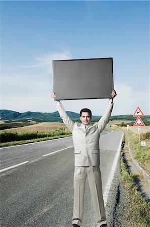 Businessman standing on the roadside and holding a sign Stock Photo - Premium Royalty-Free, Code: 630-03479314