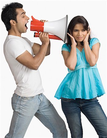 Side profile of a young man blowing a bullhorn with a teenage girl covering her ears Stock Photo - Premium Royalty-Free, Code: 630-03479394