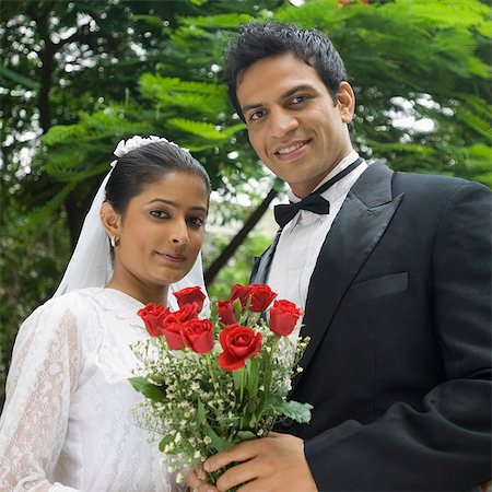 Portrait of a newlywed couple holding a bouquet of flowers and smiling Stock Photo - Premium Royalty-Free, Code: 630-03479517