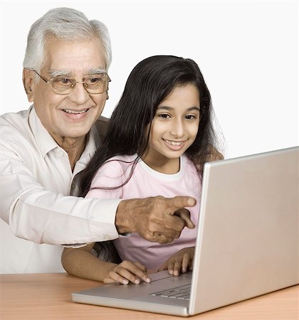 Homme senior à l'aide d'un ordinateur portable avec sa petite-fille et souriant Photographie de stock - Premium Libres de Droits, Code: 630-03479585