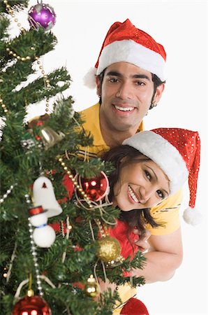 Portrait d'un couple furtivement à travers un arbre de Noël et souriant Photographie de stock - Premium Libres de Droits, Code: 630-03480397