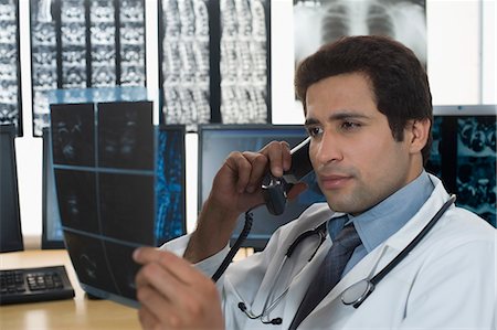 Male doctor examining an X-Ray and talking on the telephone Foto de stock - Royalty Free Premium, Número: 630-03480733