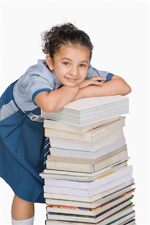 Schoolgirl leaning on a stack of books and smiling Stock Photo - Premium Royalty-Free, Code: 630-03481172
