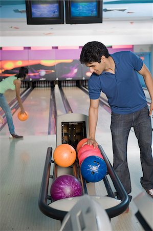 simsearch:630-03481667,k - Young man picking a bowling ball and a young woman bowling in a bowling alley Foto de stock - Royalty Free Premium, Número: 630-03481643