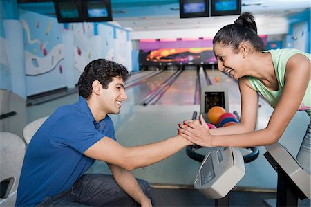 simsearch:630-03481569,k - Young man sitting near the control panel and a young woman holding his hand in a bowling alley Stock Photo - Premium Royalty-Free, Code: 630-03481657