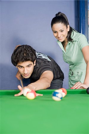 pool cue - Young man playing pool and a young woman watching his game Stock Photo - Premium Royalty-Free, Code: 630-03481688