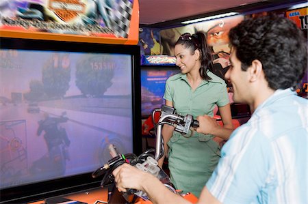 racing motor bikes photos - Young man playing video game and a young woman watching his game in a video arcade Stock Photo - Premium Royalty-Free, Code: 630-03481705