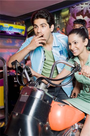 riding a friend on the handlebars - Young woman playing video game and a young man watching her game in a video arcade Stock Photo - Premium Royalty-Free, Code: 630-03481711