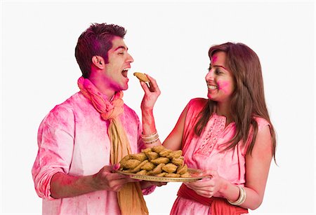 photo of a woman feeding her husband food - Couple celebrating Holi with plate of gujiyas Stock Photo - Premium Royalty-Free, Code: 630-03483135