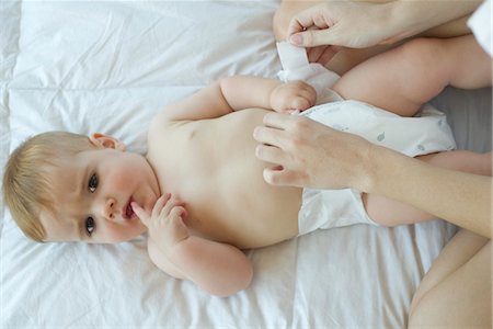 sanitario - Baby having diaper changed, looking at camera with finger in mouth Foto de stock - Sin royalties Premium, Código: 632-05554008