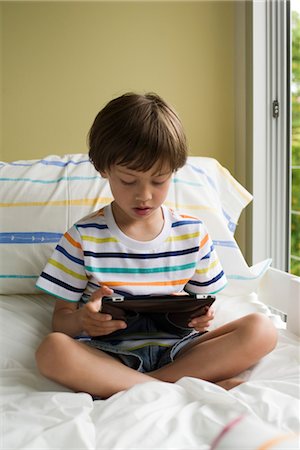 Boy sitting on bed, reading e-book Stock Photo - Premium Royalty-Free, Code: 632-05553520