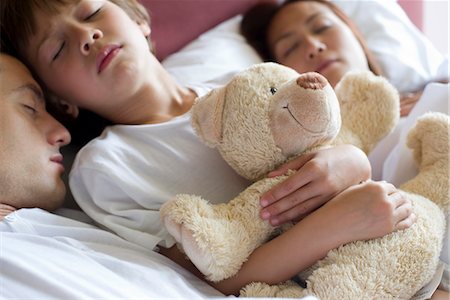 Boy sleeping in bed with his parents, holding teddy bear Foto de stock - Royalty Free Premium, Número: 632-05553614