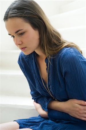 simsearch:633-05401481,k - Young woman clutching stomach, looking down in thought Stock Photo - Premium Royalty-Free, Code: 632-05553637