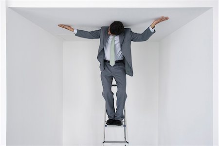 photo of frustrated businessman - Executive standing on stepladder, arms outstretched on ceiling Stock Photo - Premium Royalty-Free, Code: 632-05604359