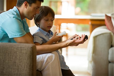 father explain child - Father and son playing video game using wireless controllers Stock Photo - Premium Royalty-Free, Code: 632-05603784