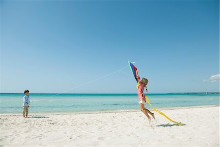 Boy flying kite on beach, girl jumping to catch Stock Photo - Premium Royalty-Free, Code: 632-05759456