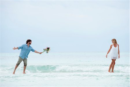 Couple walking apart in sea, man holding out bouquet Stock Photo - Premium Royalty-Free, Code: 632-05759725