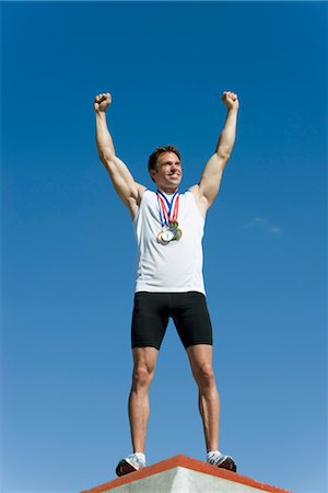 Male athlete standing on winner's podium with arms raised in victory Stock Photo - Premium Royalty-Free, Code: 632-05759997