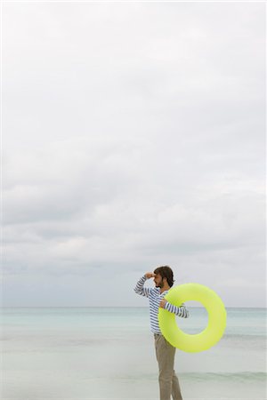 simsearch:632-06318057,k - Young man carrying inflatable swimming ring, looking into distance Stock Photo - Premium Royalty-Free, Code: 632-05760300