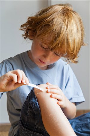 Boy removing adhesive bandage from knee Stock Photo - Premium Royalty-Free, Code: 632-05816105