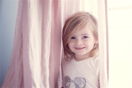 shy children - Little girl in front of window, smiling, portrait Stock Photo - Premium Royalty-Free, Code: 632-05816407