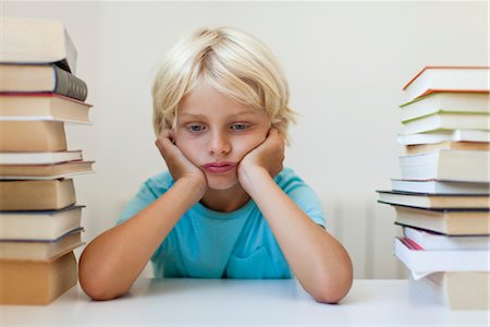 Boy sitting between two stacks of books, sulking Foto de stock - Sin royalties Premium, Código: 632-05816528