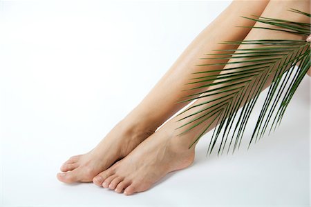 Woman holding palm frond against bare legs, cropped Stock Photo - Premium Royalty-Free, Code: 632-05817039