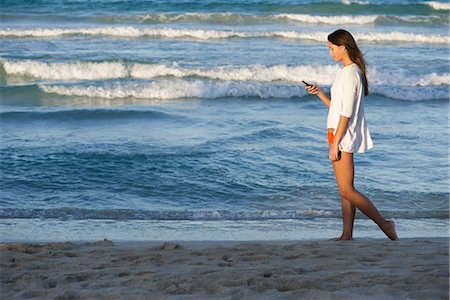 Young woman using cell phone while strolling on beach, side view Stock Photo - Premium Royalty-Free, Code: 632-05817047