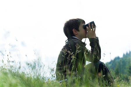 simsearch:633-05401634,k - Boy sitting in meadow looking through binoculars Fotografie stock - Premium Royalty-Free, Codice: 632-05845295