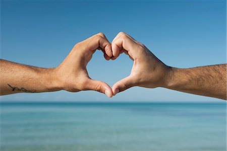 romantic hand - Two men's hands forming heart shape by ocean, cropped Stock Photo - Premium Royalty-Free, Code: 632-05845402