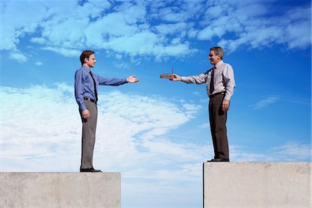 Businessmen standing on platforms, one handing the other a tiny factory Stock Photo - Premium Royalty-Free, Code: 632-06029333