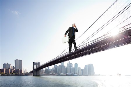 sun urban people - Giant businessman carrying briefcase stuffed with money across bridge Stock Photo - Premium Royalty-Free, Code: 632-06030026