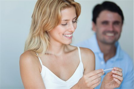 simsearch:632-06030195,k - Smiling young woman holding pregnancy test, man in background Fotografie stock - Premium Royalty-Free, Codice: 632-06030032