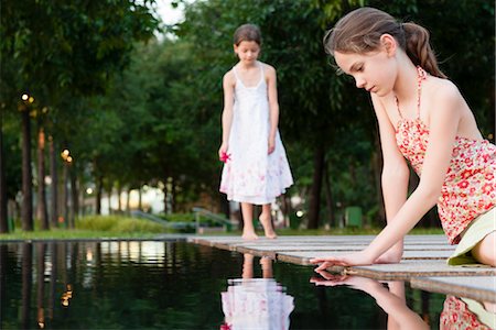 preteen girls dresses pictures - Girl sitting by edge of pond touching surface of water, another girl in background Stock Photo - Premium Royalty-Free, Code: 632-06030047