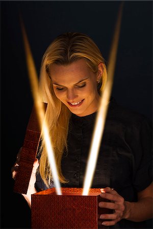 female holding christmas present - Woman illuminated by beams of light as she opens gift Stock Photo - Premium Royalty-Free, Code: 632-06118428