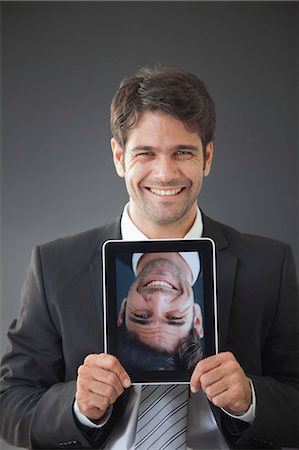 picture within picture - Man holding up digital tablet displaying upside down image of himself smiling Stock Photo - Premium Royalty-Free, Code: 632-06118567