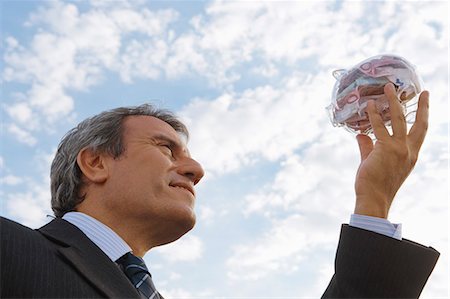 piggy bank, savings - Mature man holding up transparent piggy bank filled with euros Stock Photo - Premium Royalty-Free, Code: 632-06118645