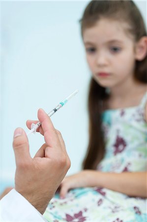 Doctor's hand holding syringe, girl sitting in background Foto de stock - Sin royalties Premium, Código: 632-06317074