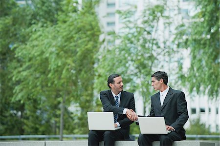 Business executives sitting outdoors with laptop computers, shaking hands Stock Photo - Premium Royalty-Free, Code: 632-06317227