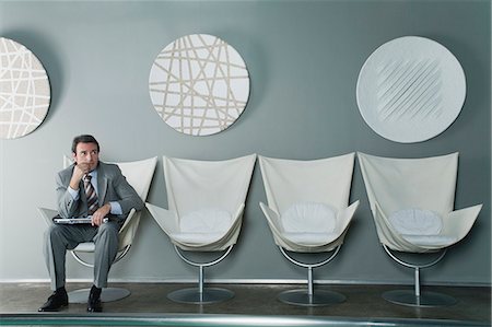 Mature businessman sitting at end of row of chairs in waiting room Stock Photo - Premium Royalty-Free, Code: 632-06317346