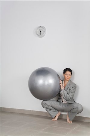 Young businesswoman crouching against wall holding fitness ball Stock Photo - Premium Royalty-Free, Code: 632-06317368