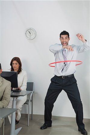 Young businessman playing with hula hoop in office while colleagues work Stock Photo - Premium Royalty-Free, Code: 632-06317465