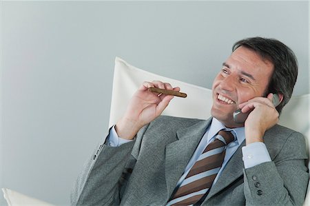 Mature businessman using cell phone and smoking cigar Stock Photo - Premium Royalty-Free, Code: 632-06317516