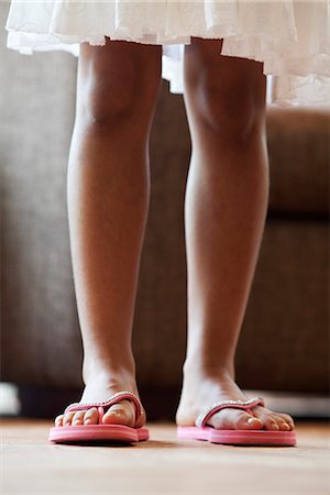 Low section of teenage girl wearing flip-flops sitting on tree trunk Stock  Photo