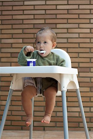 Bébé fille assis dans la chaise haute, manger un yaourt avec une cuillère Photographie de stock - Premium Libres de Droits, Code: 632-06317797