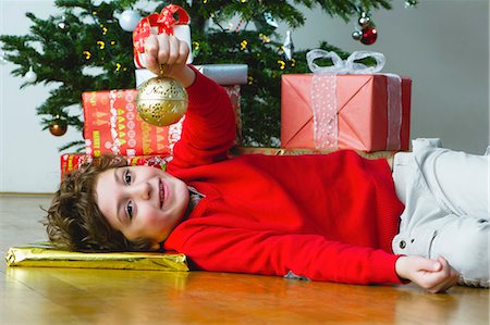 simsearch:632-06354083,k - Boy lying on floor by Christmas tree, holding up ornament Fotografie stock - Premium Royalty-Free, Codice: 632-06354155